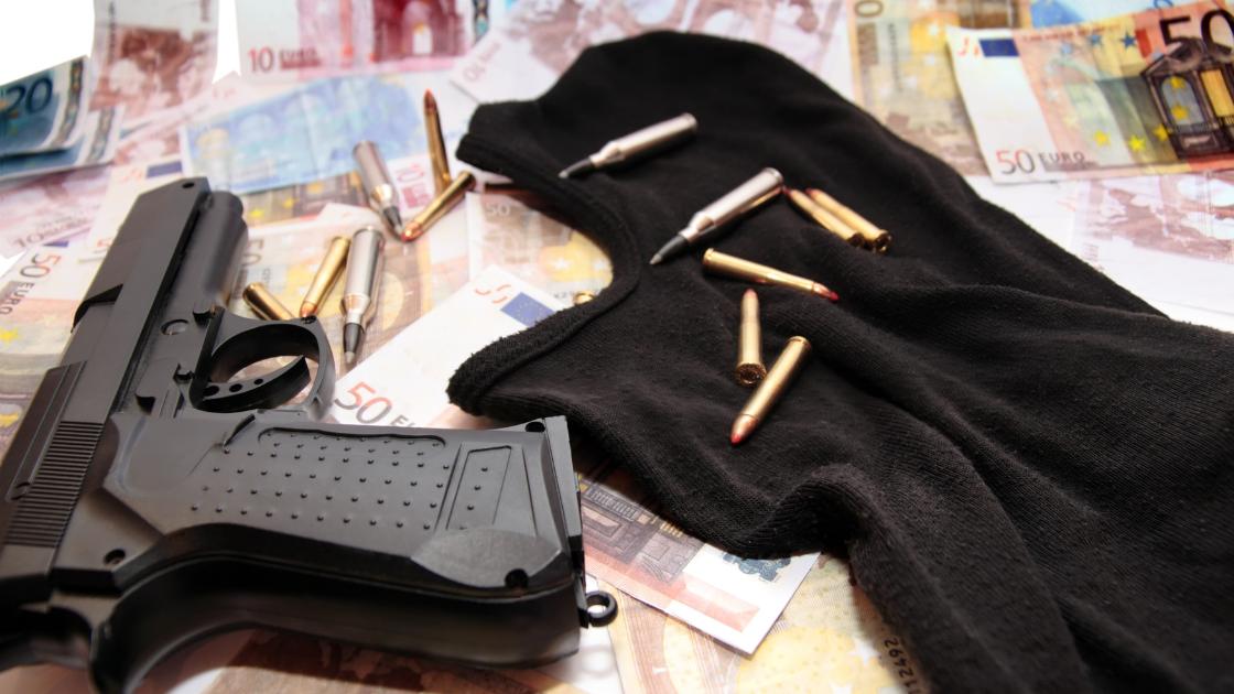 Riciclaggio di denaro inverso: una pistola con proiettili e una maschera sopra il denaro.